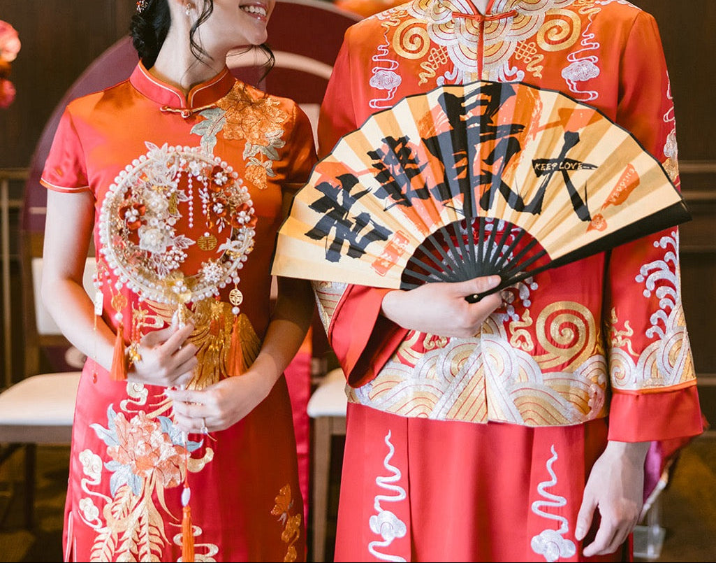 Two people in traditional Chinese attire with a fan, indoors.