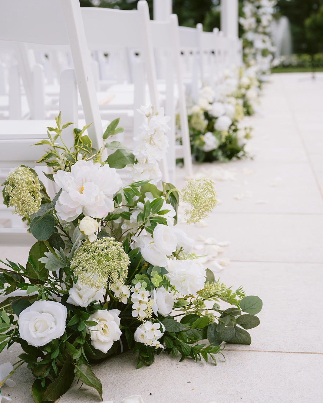 White flowers and greenery arranged along a white aisle with chairs.