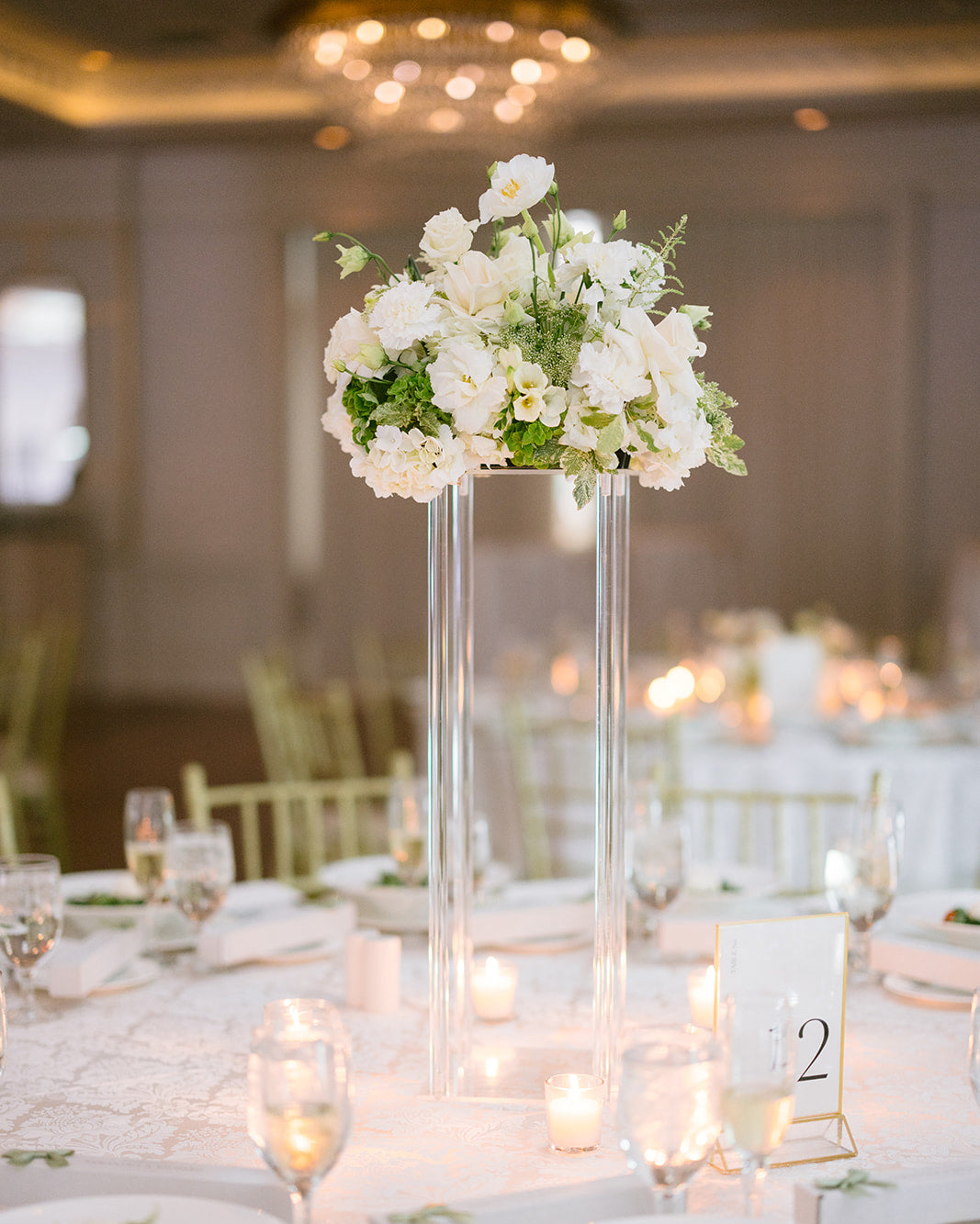 Floral centerpiece on a tall clear vase with candles and table settings in a banquet hall.