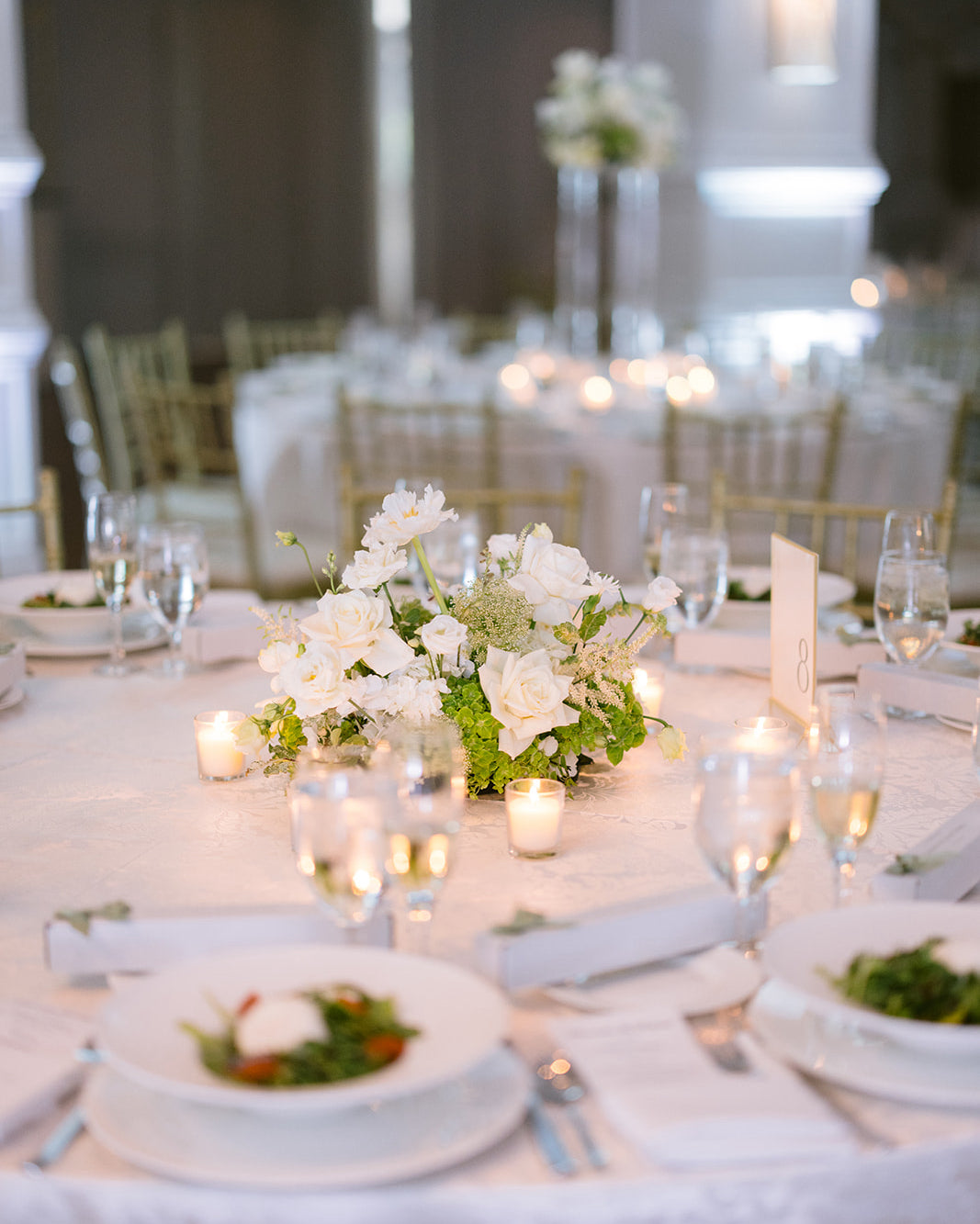 Elegant table setting with white flowers, candles, and greenery in a formal dining room.