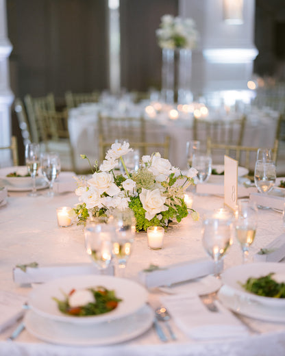 Elegant table setting with white flowers, candles, and greenery in a formal dining room.