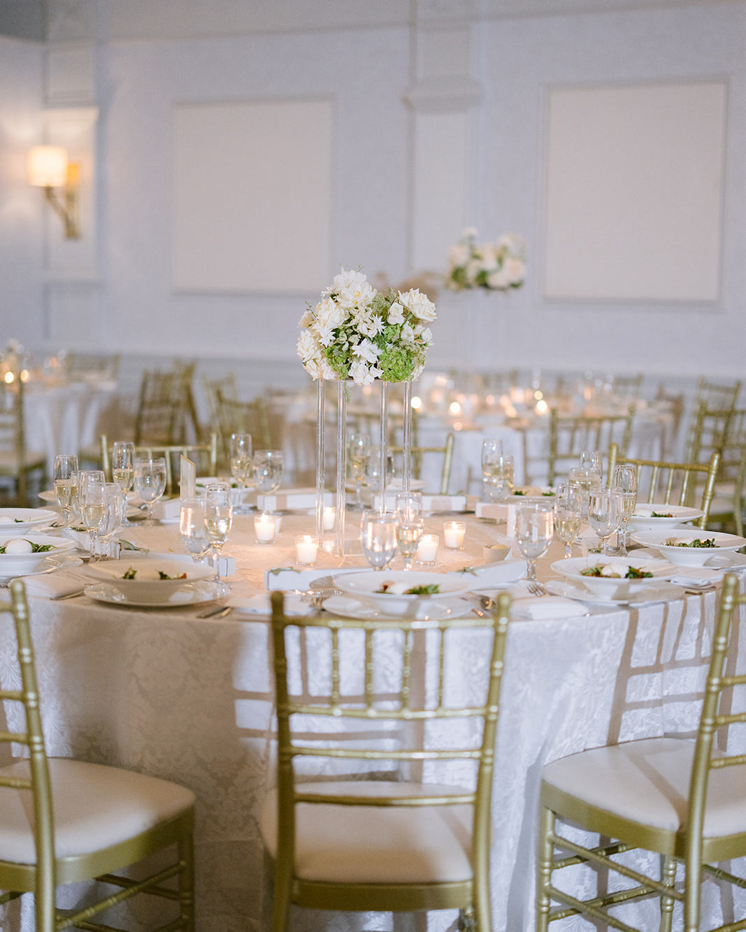 Elegant banquet hall with round tables, white tablecloths, gold chairs, and floral centerpieces.