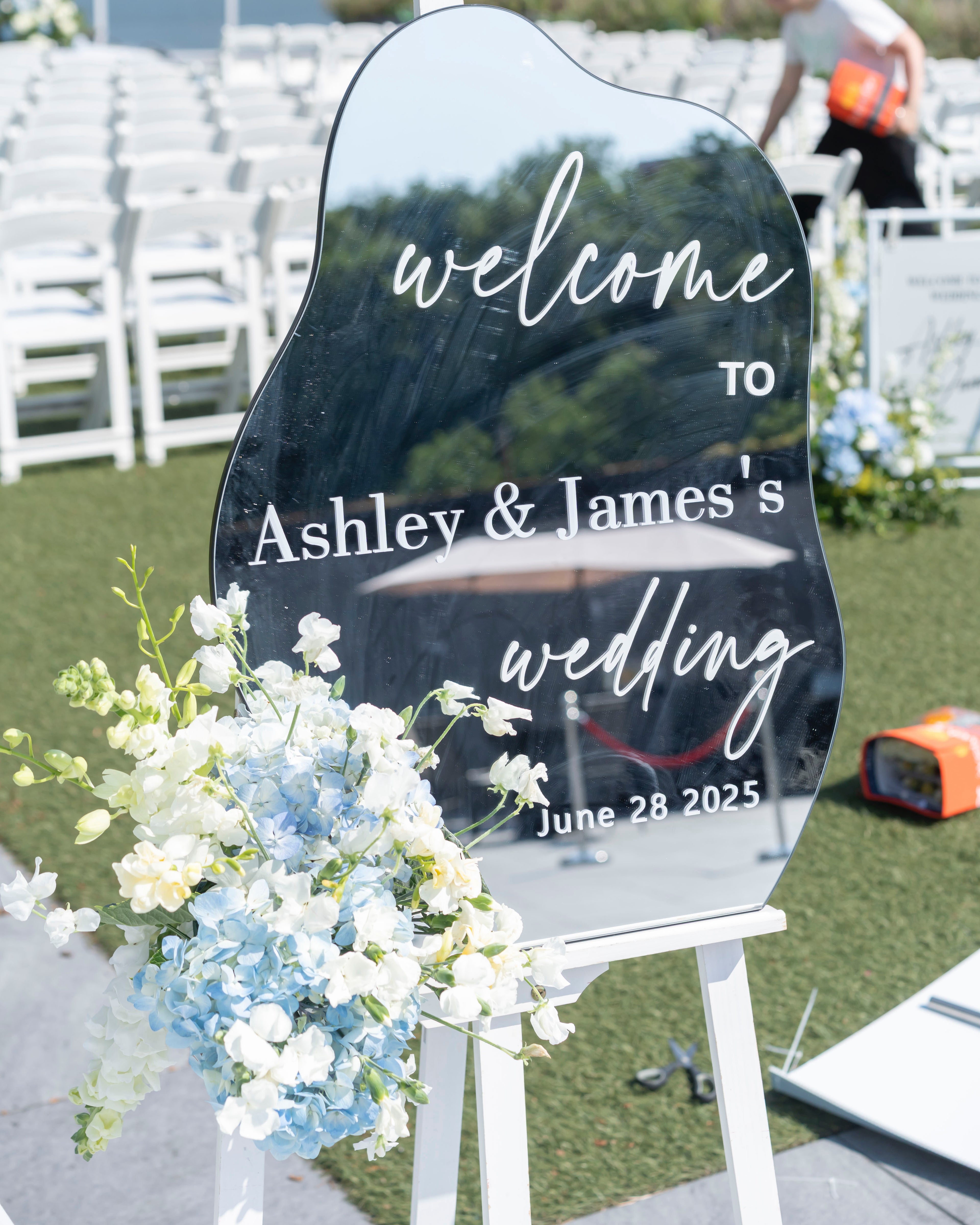Wedding welcome sign for Ashley &amp; James with floral decorations on a grassy area.