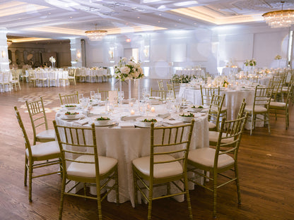 Dining hall with tables set for a formal event, featuring white tablecloths and gold chairs.