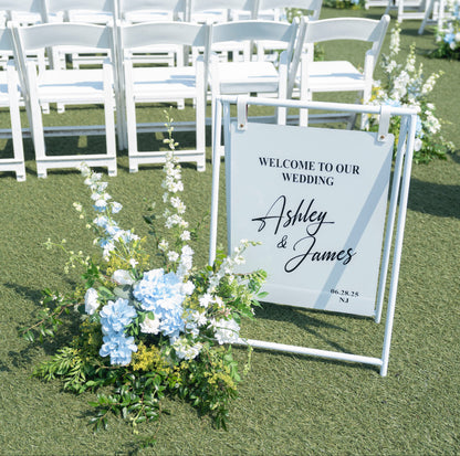 Wedding setup with white chairs, floral arrangements, and a welcome sign on a rooftop with cityscape in the background.