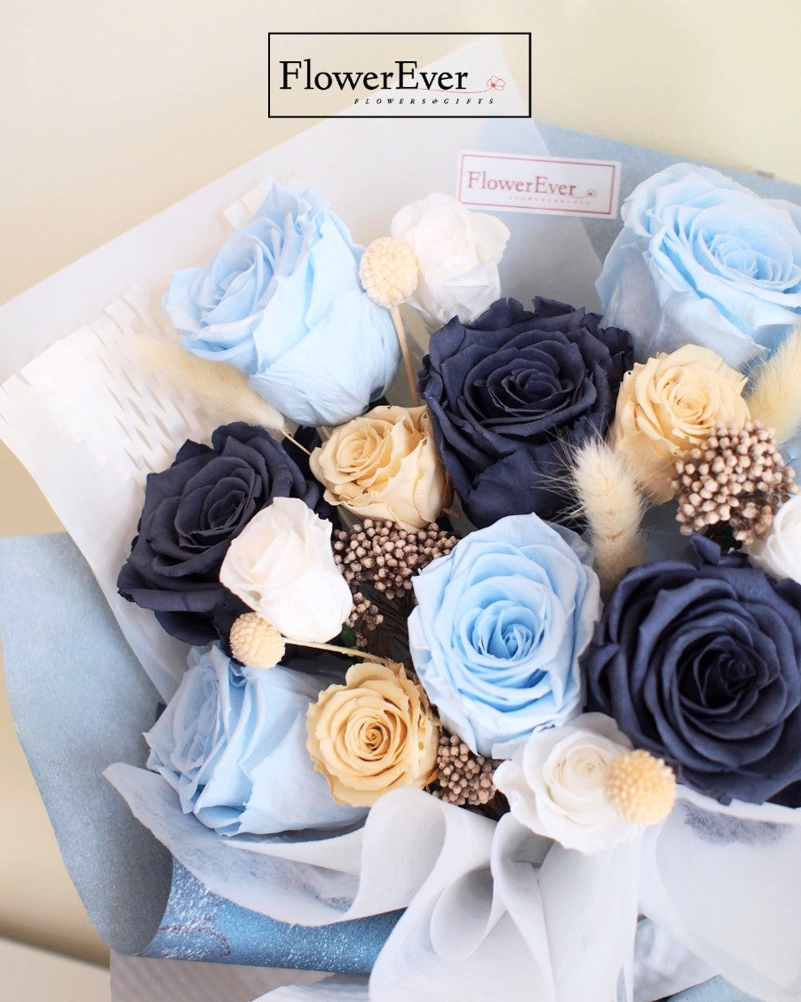 Twelve preserved rose stems in shades of blue mixed with nude and white flowers arranged in a colorful hand-tied bouquet.