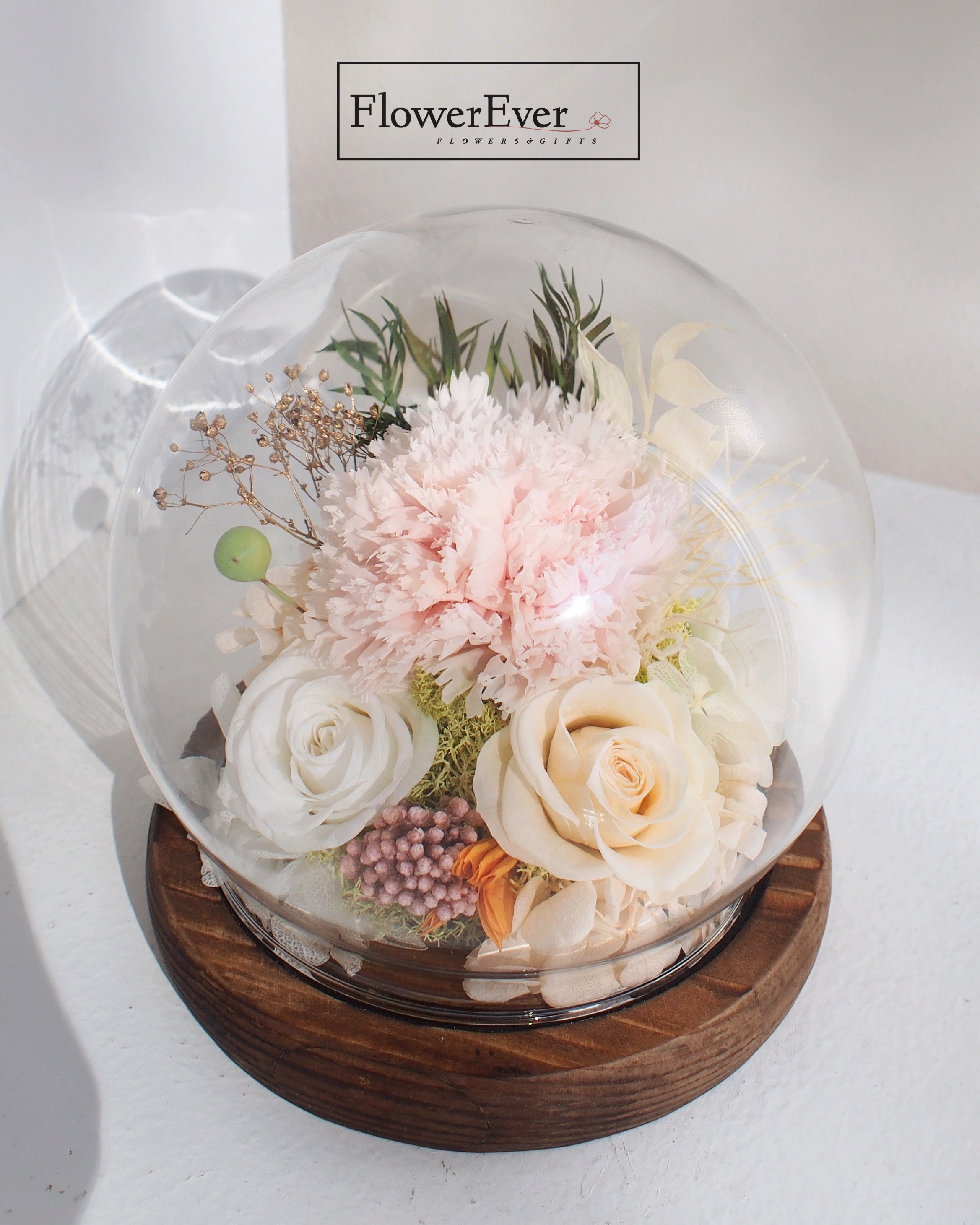 A preserved Pink carnations and white roses arrangement in a glass globe