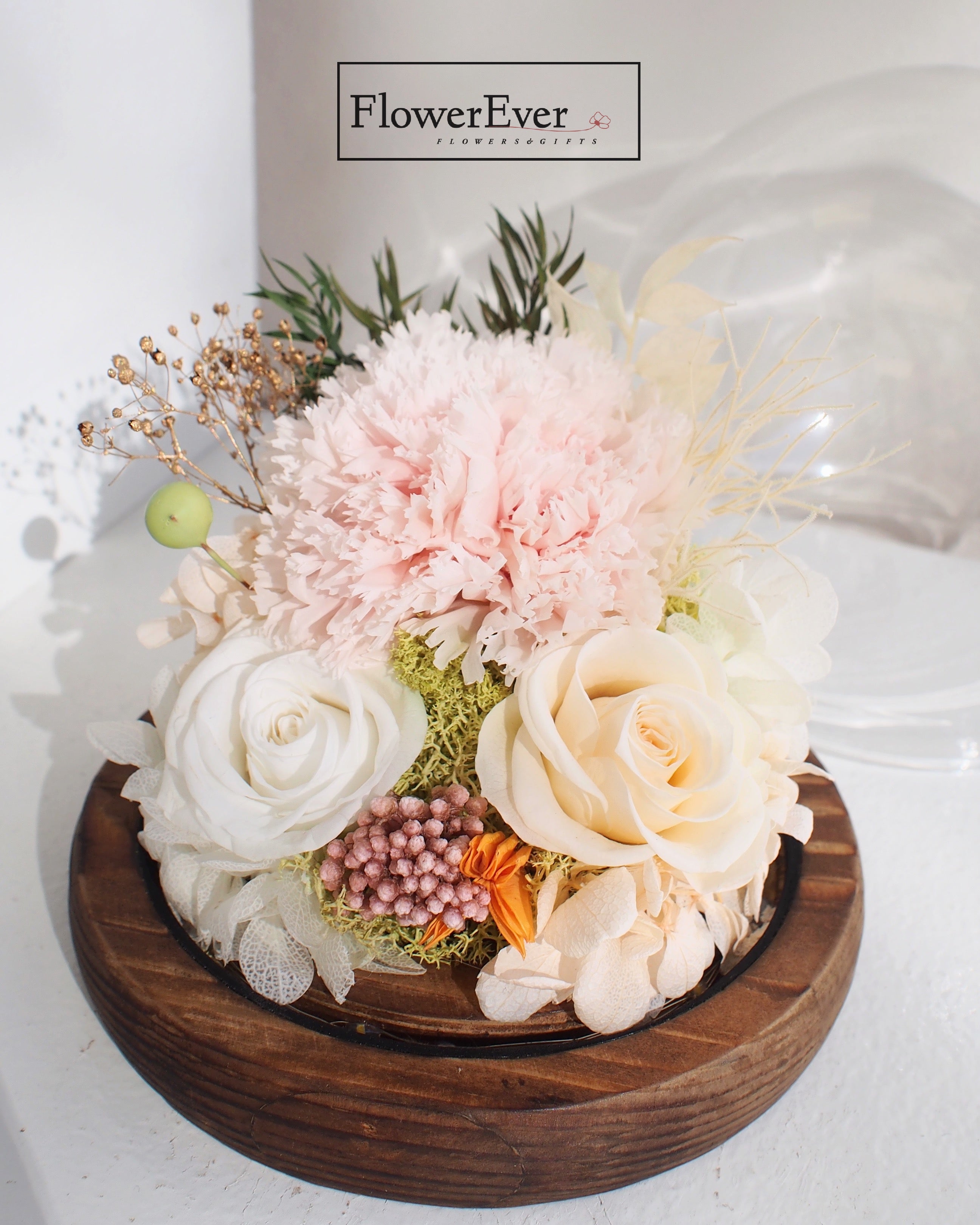 A glass dome containing vivid preserved Pink carnations and white roses