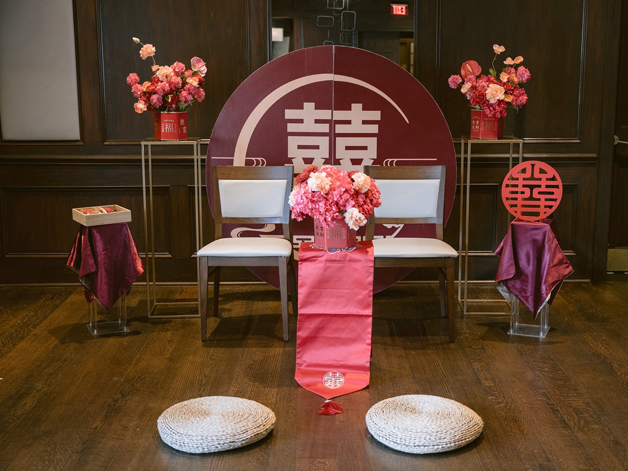 Decorated event setup with chairs, floral arrangements, and a red and white backdrop.