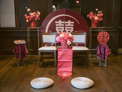Decorated event setup with chairs, floral arrangements, and a red and white backdrop.