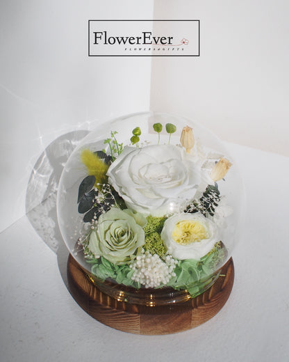 A transparent glass dome paperweight containing preserved roses in sage and white.