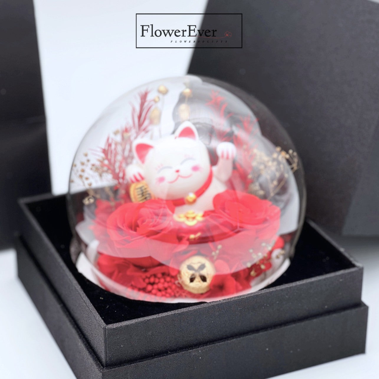 A clear glass dome with a beckoning lucky cat figurine surrounded by red preserved flowers as a grand opening gift.