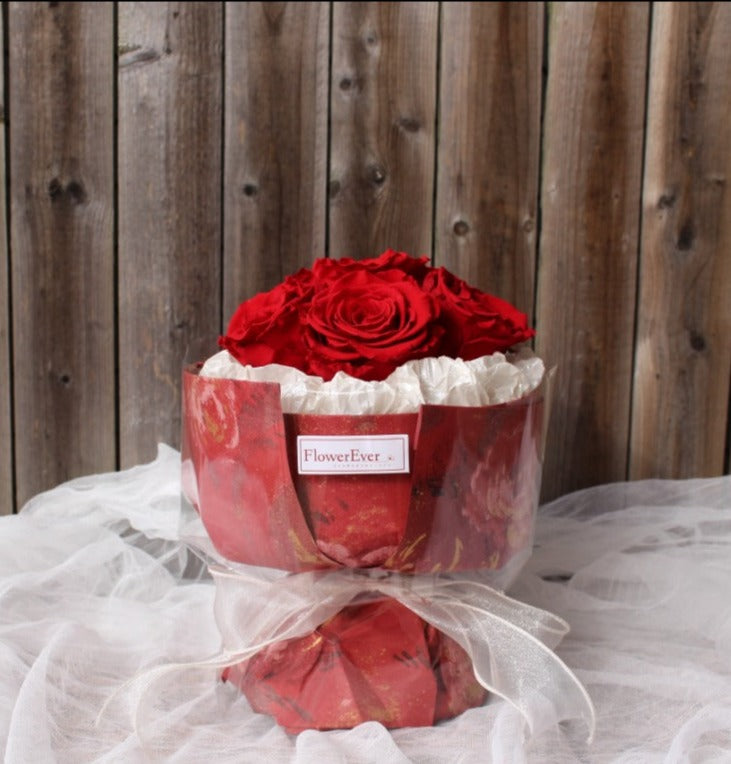 A petite Russian-style preserved flower arrangement featuring 6 stems of vivid red roses statice flowers.