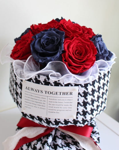 A dozen vivid red and blue preserved rose stems in a Russian style bouquet wrapped in an elegant Chanel black and white houndstooth paper.