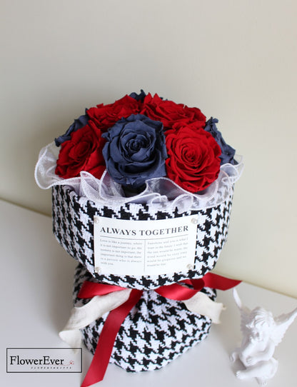 A dozen preserved vivid red and blue rose stems arranged in a Russian floral style bouquet gift wrapped in Chanel houndstooth paper.