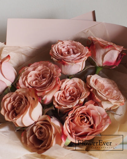 A dozen brown, beige and ivory preserved rose blooms in various stages bundled in a round cappuccino-toned floral bouquet.