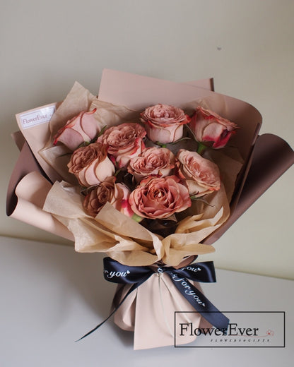 Twelve vintage style brown and white preserved roses arranged in a round bouquet evoking a cappuccino colored floral arrangement.