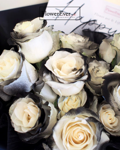 A round Russian style preserved floral arrangement with 16 stems - mix of white roses at different blooming stages and closed black rose buds.