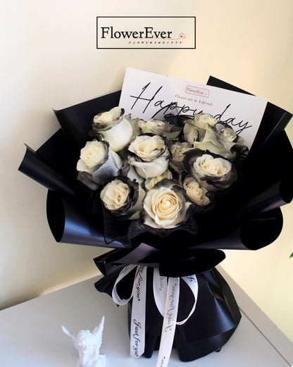 A bundle of 16 white and black preserved roses composed in a round shape floral bouquet with Russian floral style wrapped in black paper.