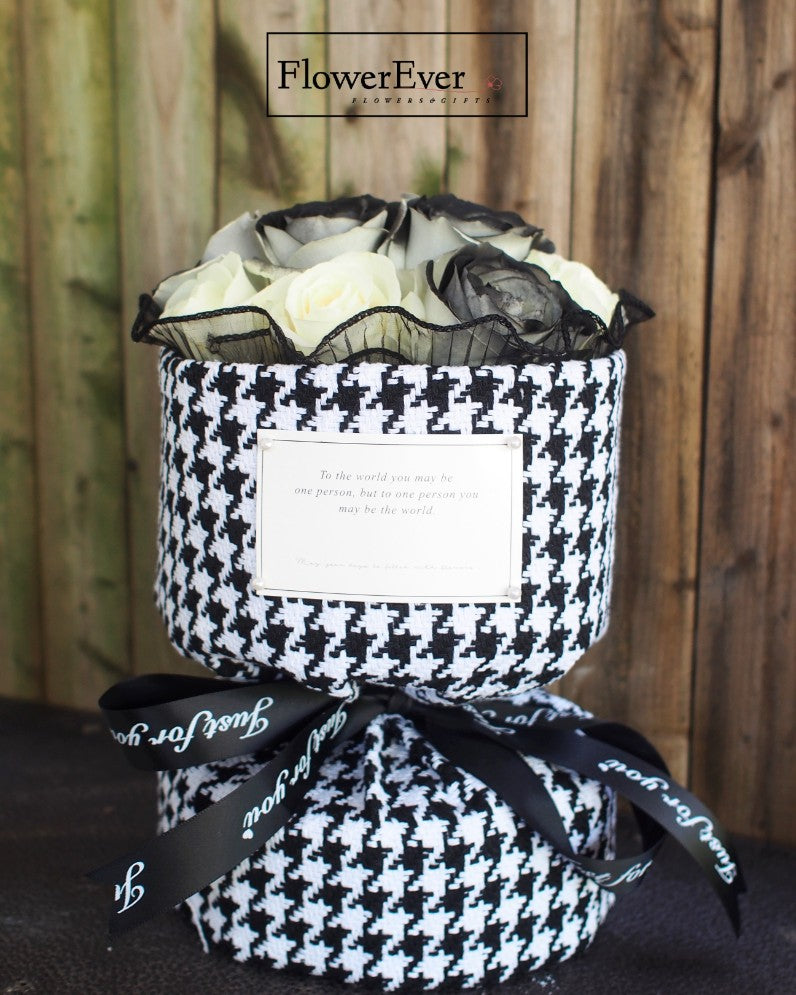 A Russian style floral arrangement with 12 stems of black and white preserved roses bundled in a Chanel branded houndstooth patterned paper