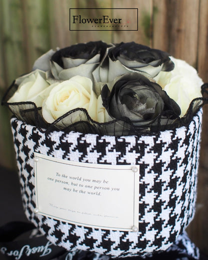 A wrapped Russian-inspired floral arrangement with 12 preserved black and white rose stems bundled elegantly in a Chanel-print houndstooth paper.