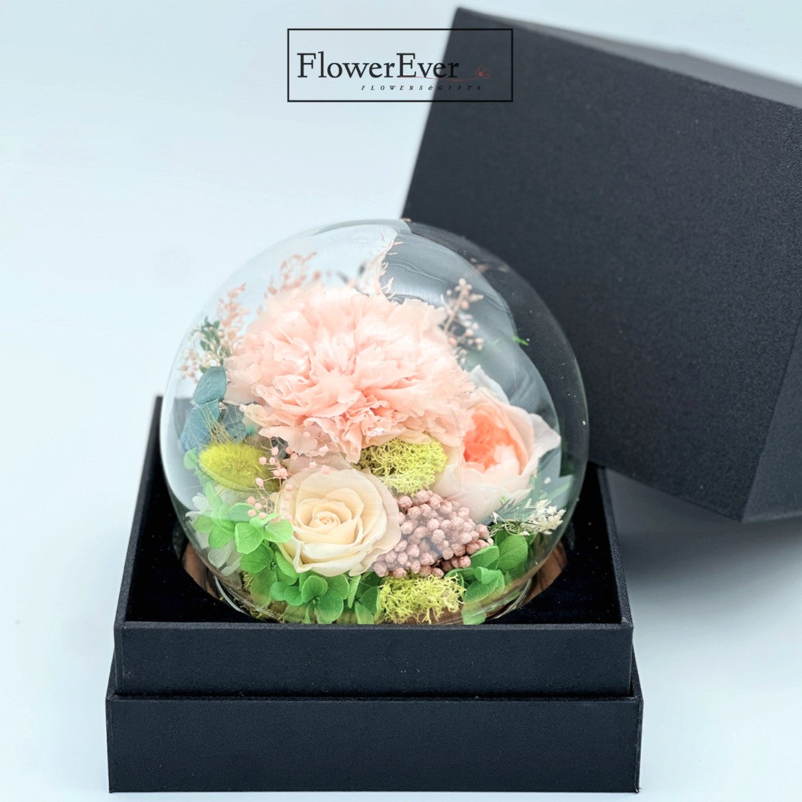 Vivid preserved carnation flowers and buds enclosed in a glass dome as a floral gift celebrating mothers.