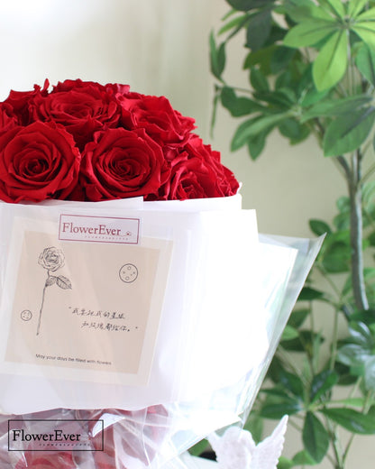 A floral arrangement of 33 vivid red preserved rose stems in a round Russian style wrapped in white paper.