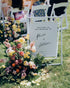 Wedding welcome sign with floral arrangement on a grassy outdoor setting