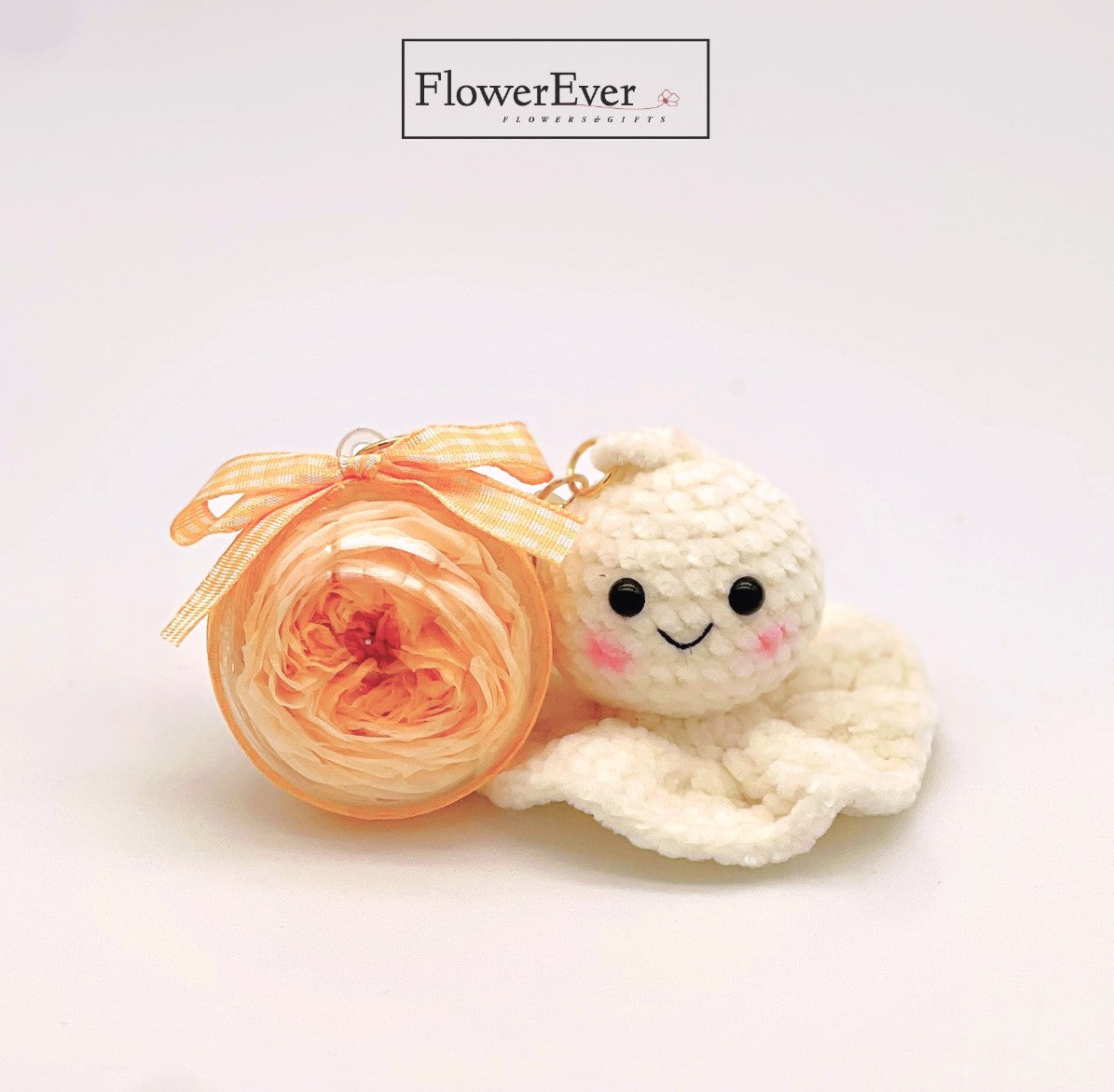 A crocheted white teru teru bozu keychain ornament with a small preserved yellow daisy flower sewn on.