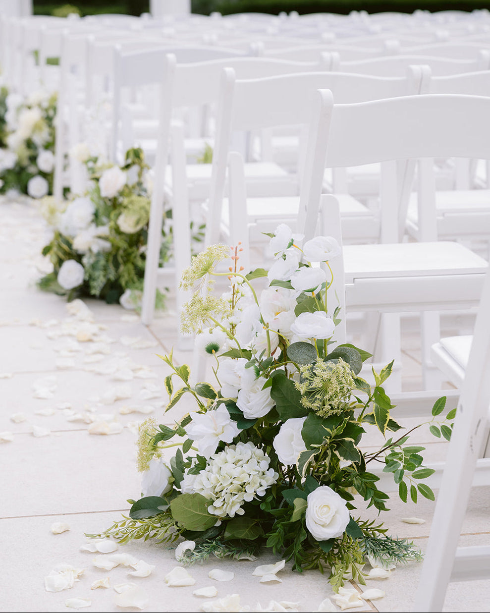 Decorative floral arrangements on white chairs at a wedding ceremony.