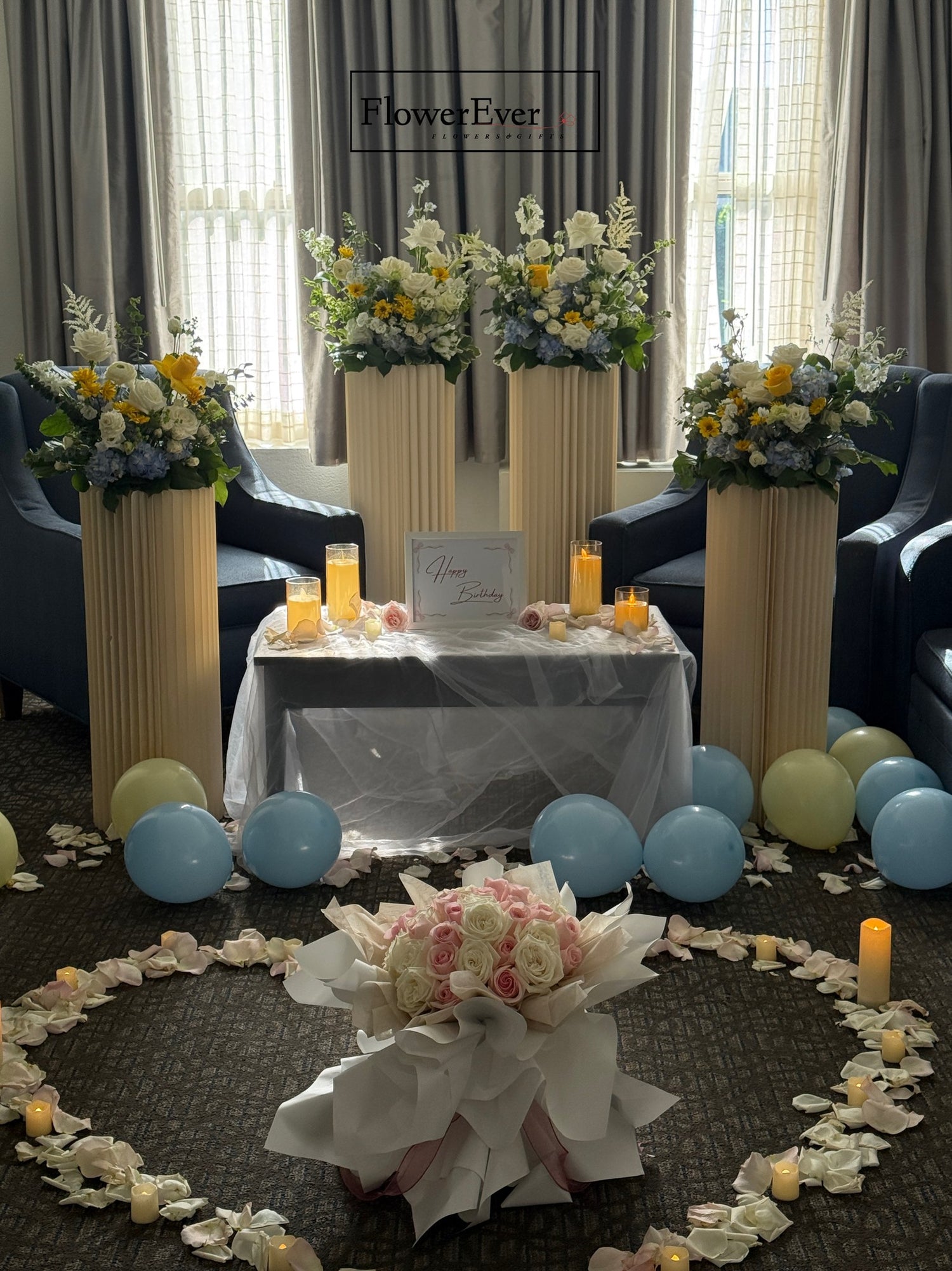Decorative setup with floral arrangements, candles, and balloons in a room.