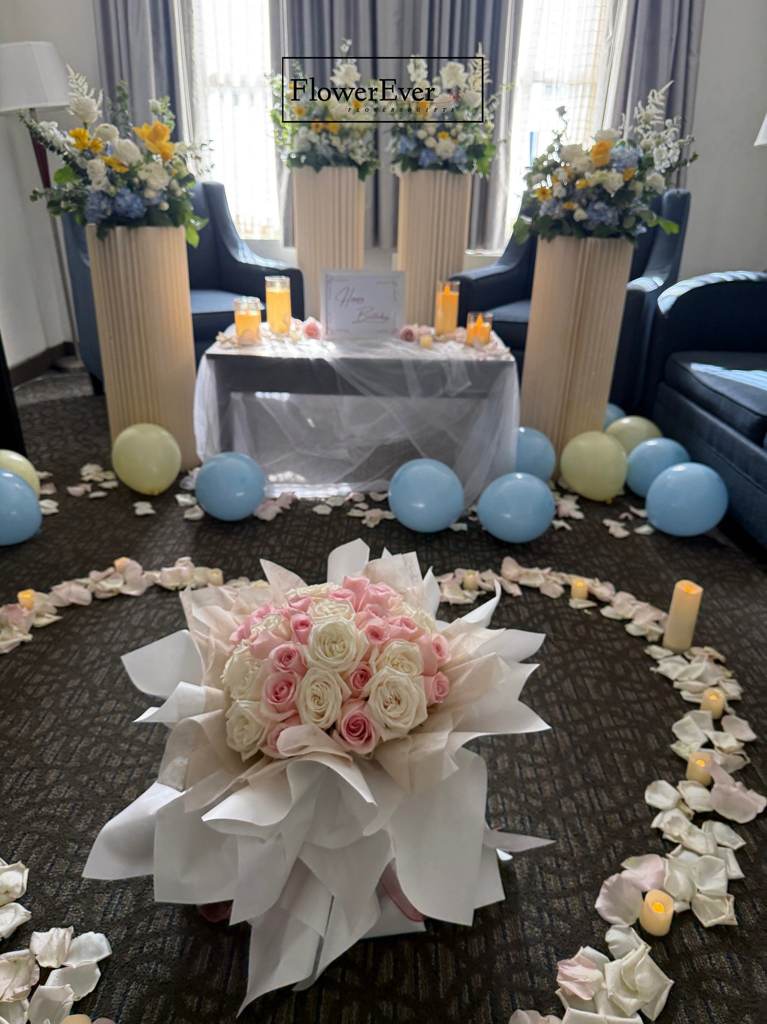 Decorative setup with flowers, balloons, and a table in a room.