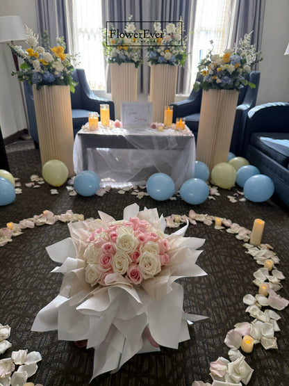 Decorative setup with flowers, balloons, and a table in a room.