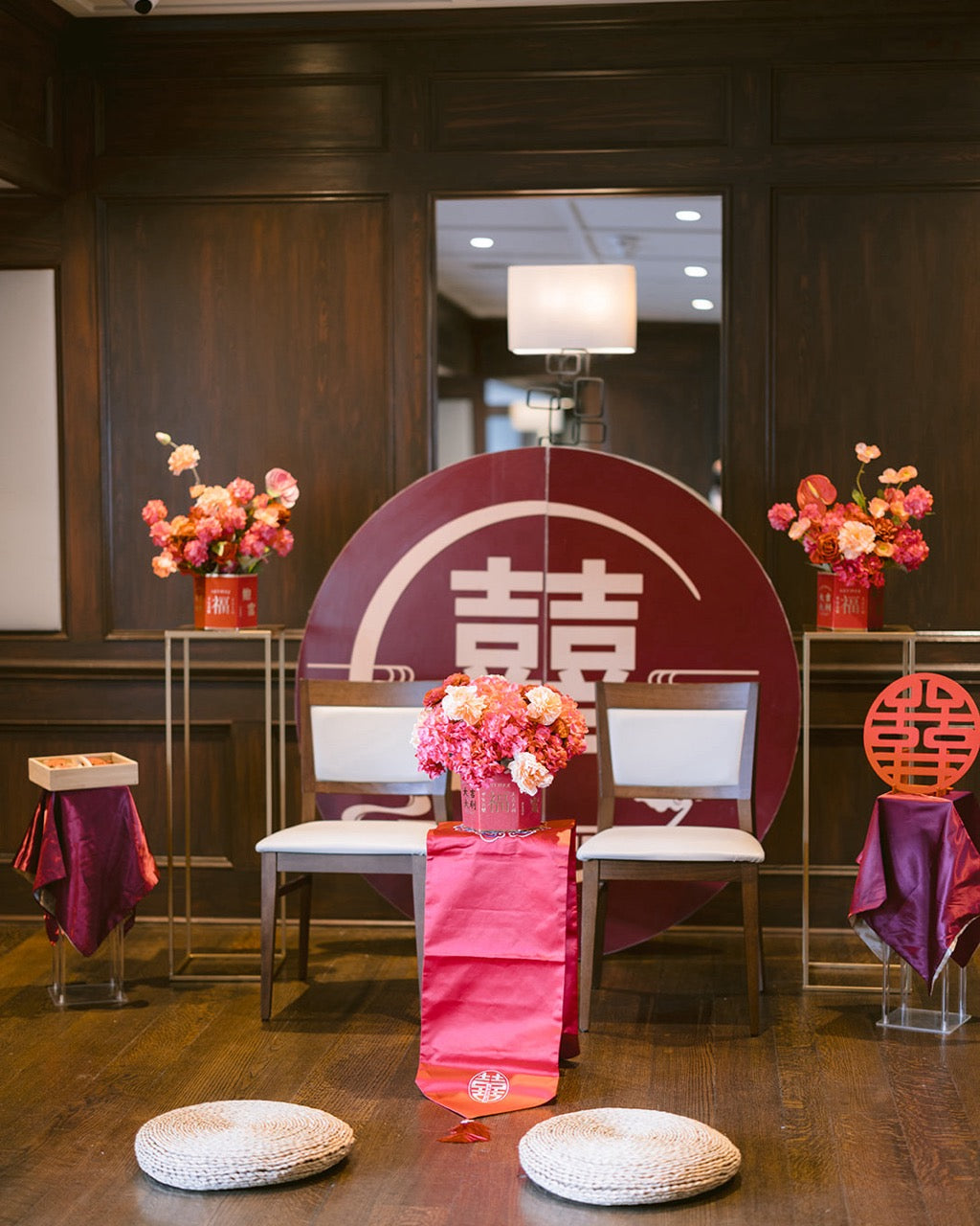 Decorative setup with floral arrangements, red and white chairs, and a large circular sign in a room.